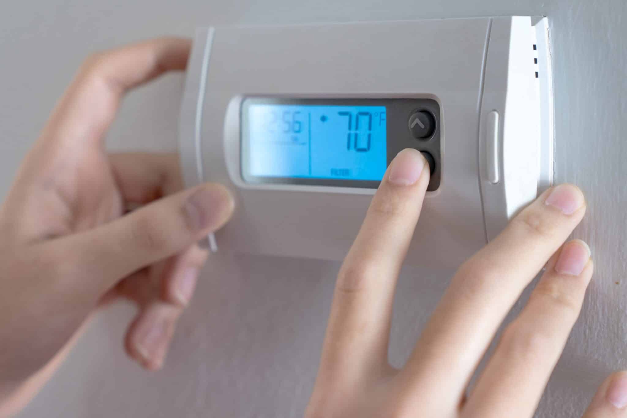 A woman is pressing the down button of a wall attached house thermostat, Thermostat Upgrades.
